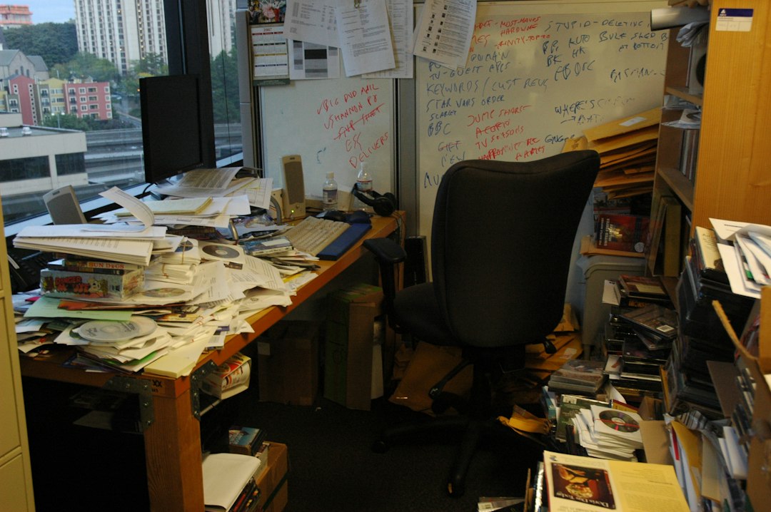 An office desk buried under piles of accreditation paperwork
