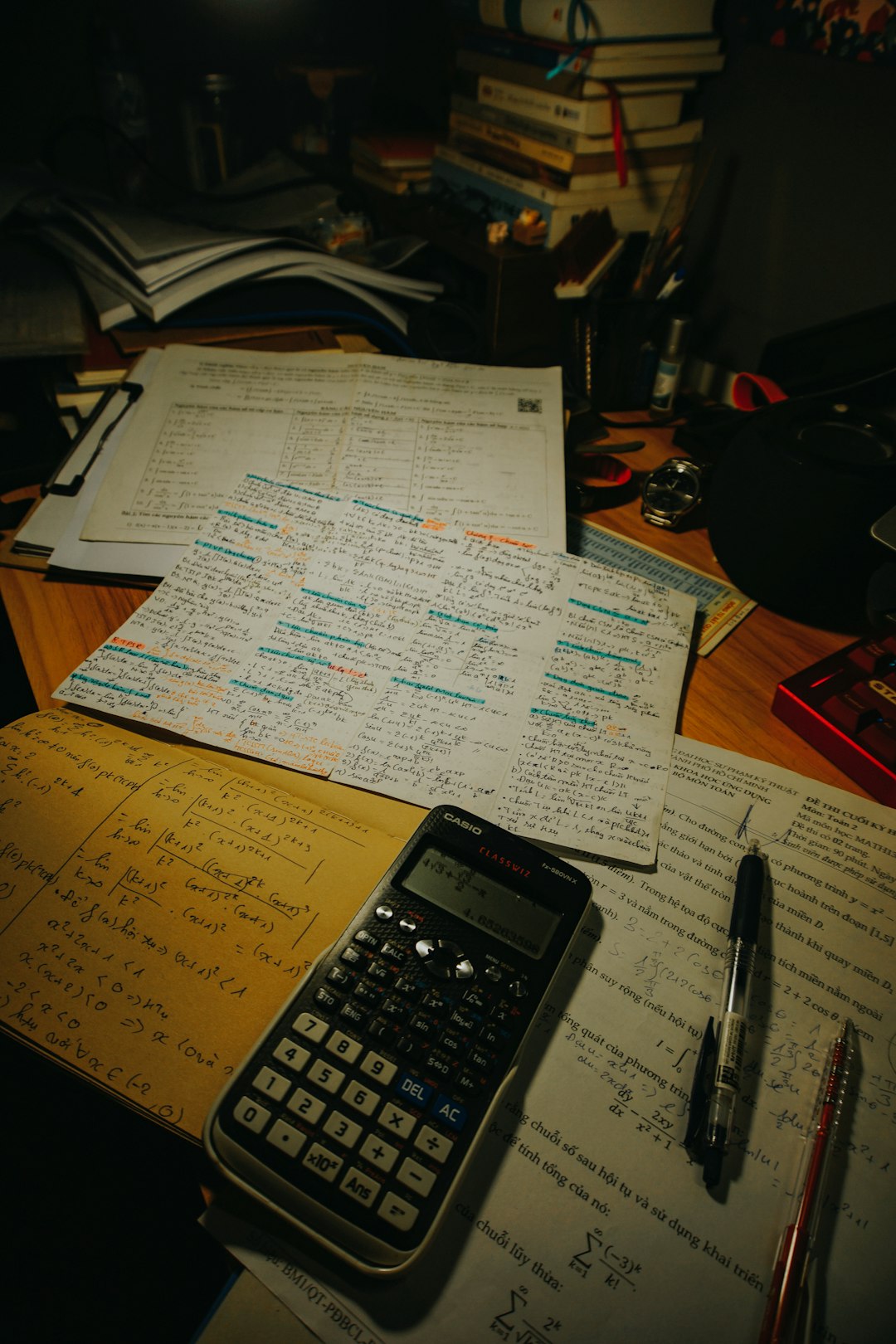Highlighted spreadsheets, a calculator, and scattered source documents on a desk