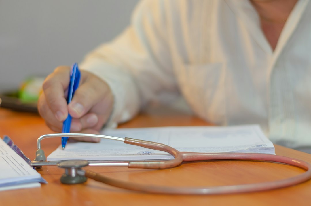 A hand writing notes with a pen next to a stethoscope on a desk