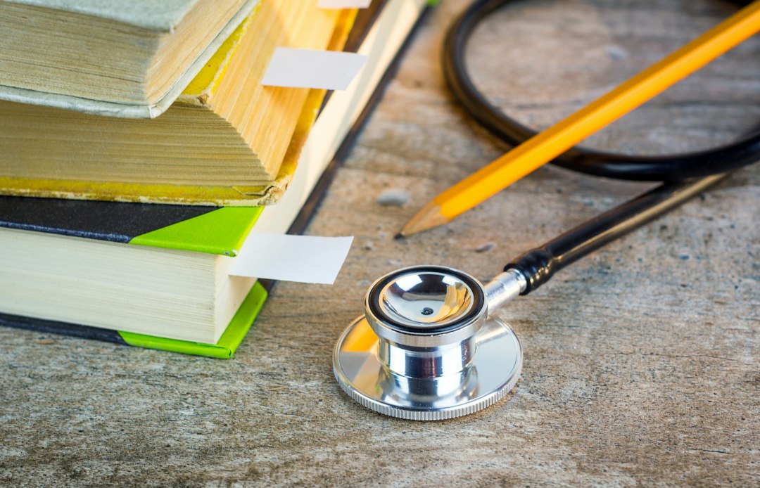 A stethoscope resting on a stack of textbooks and a pencil, the standards and curriculum behind entry-level competency