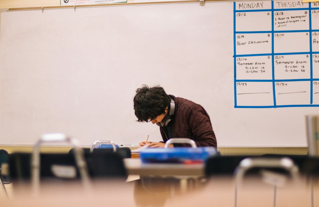 A student writing on paper at a desk in an empty classroom