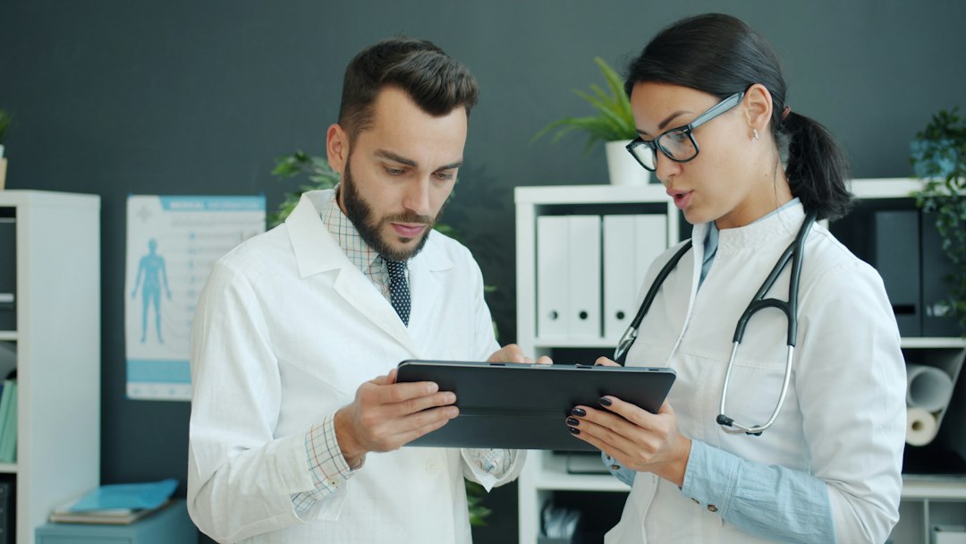Two clinicians in white coats reviewing a competency record on a tablet together